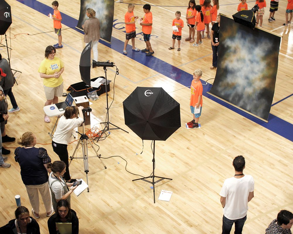 Picture day in a school gym: students lined up while a boy is photographed