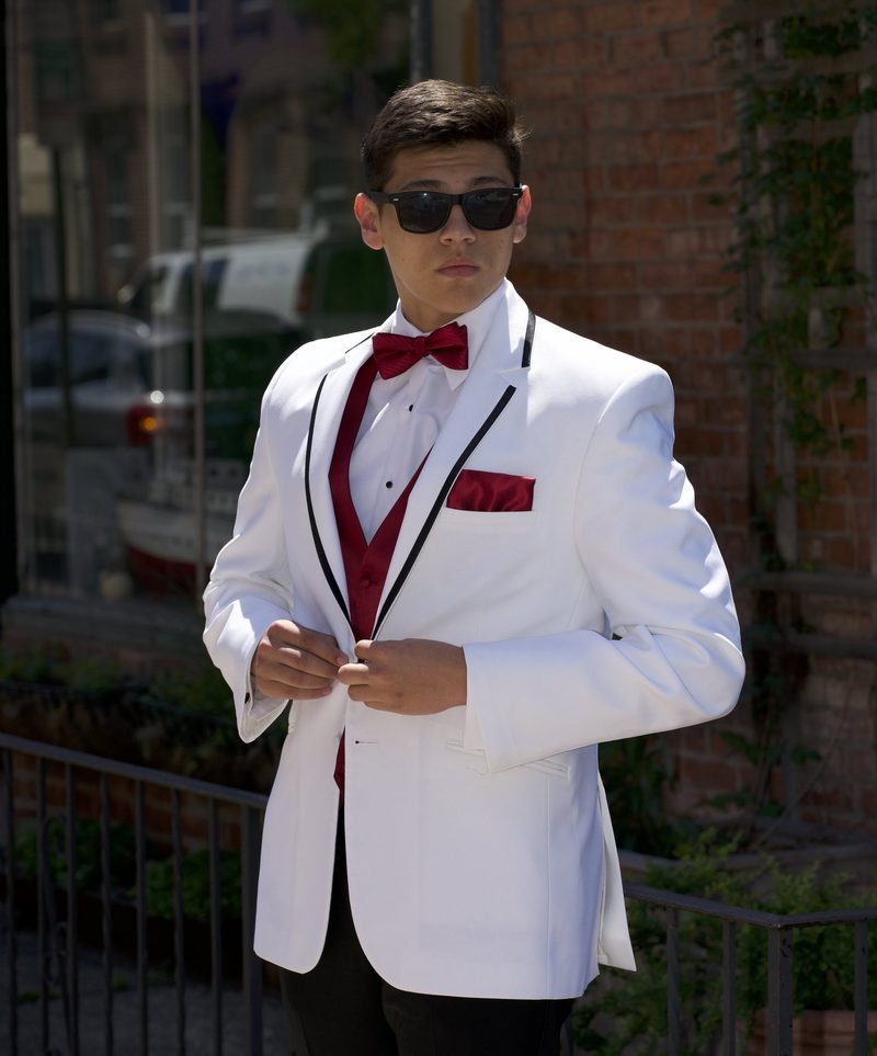 Boy in a white tuxedo and sunglasses posing on a city sidewalk