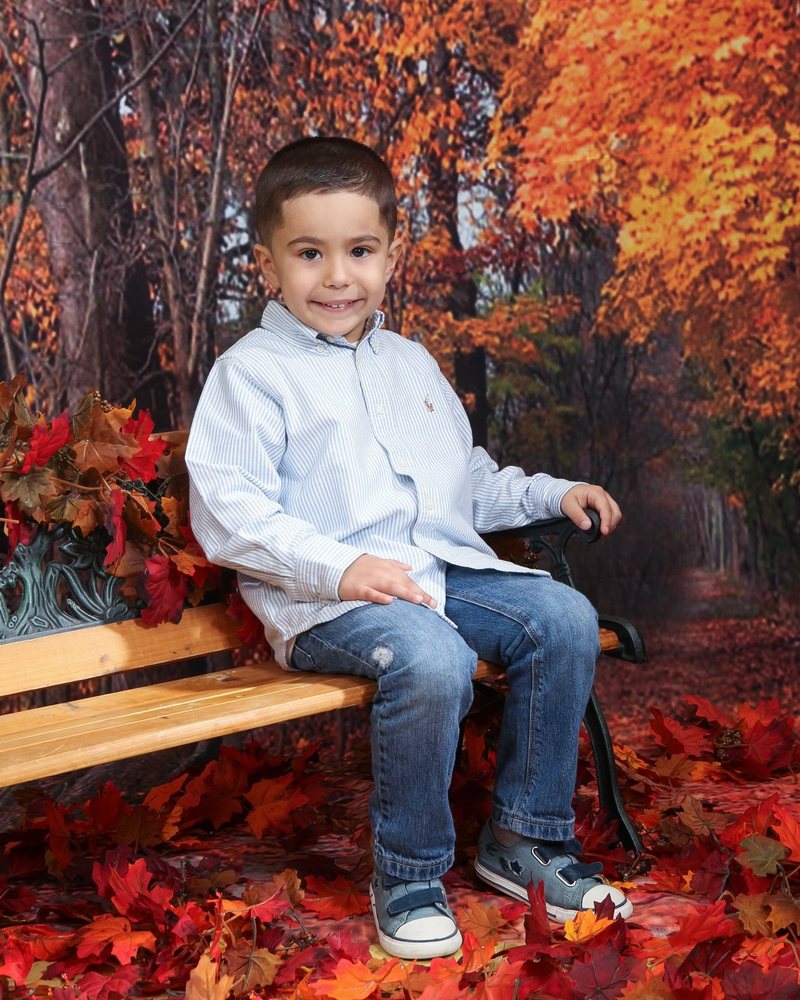 Boy in a light blue shirt sitting on a bench in an autumn scene