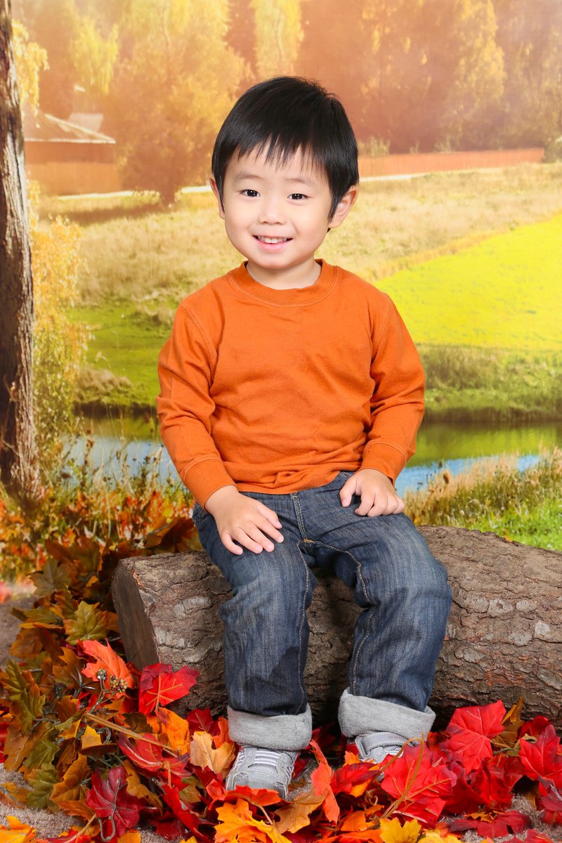 Boy in an orange shirt sitting on a log among autumn leaves