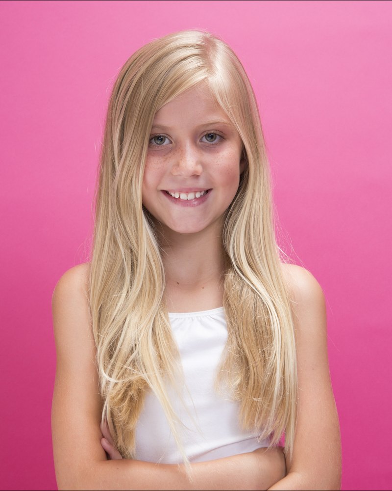 Girl with long blonde hair smiling with her arms crossed on a pink backdrop