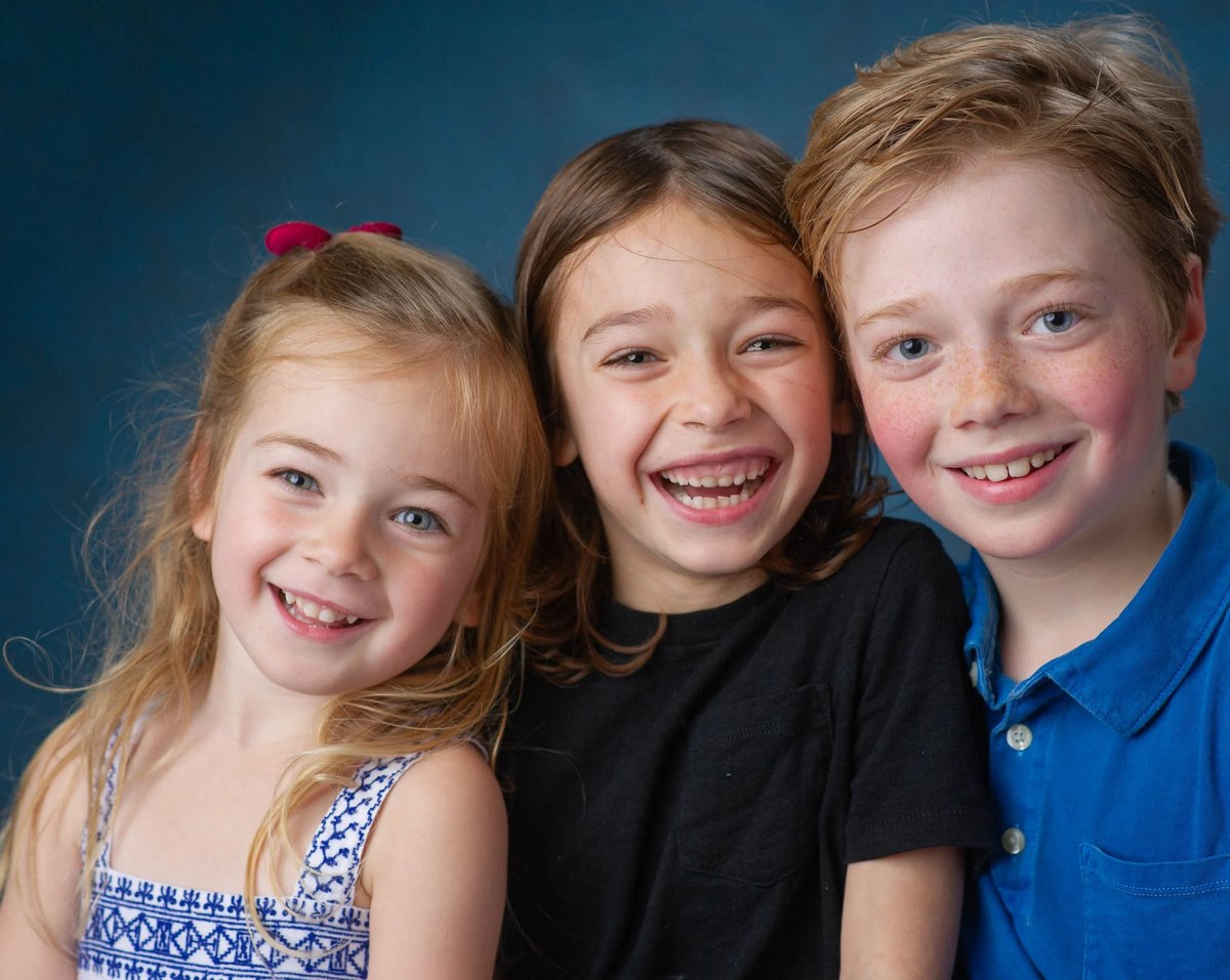 Three siblings laughing together in a studio portrait
